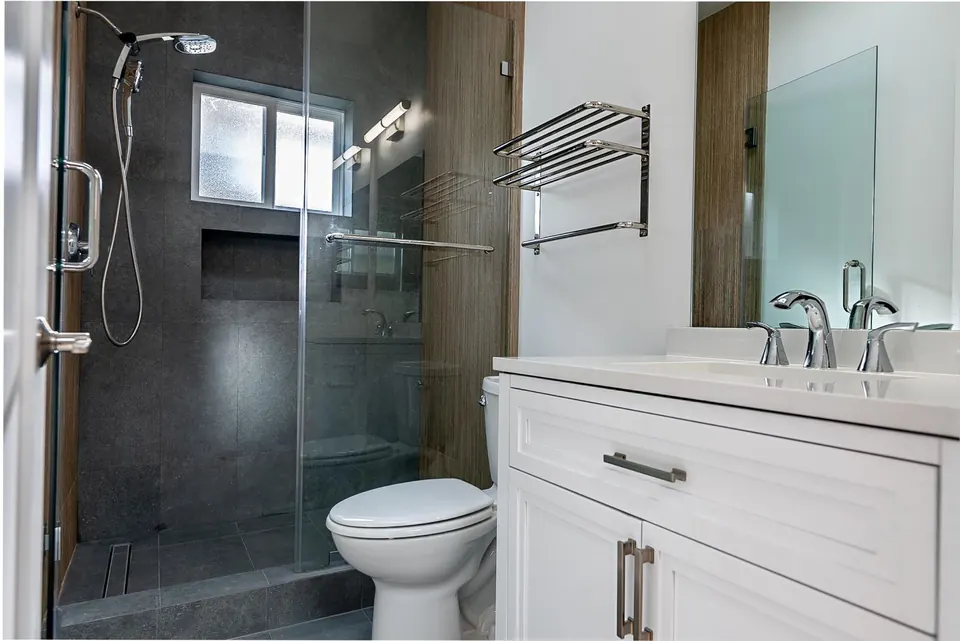 ADU bathroom with a charcoal-tile shower behind frameless glass, a chrome towel rack and a white shaker vanity