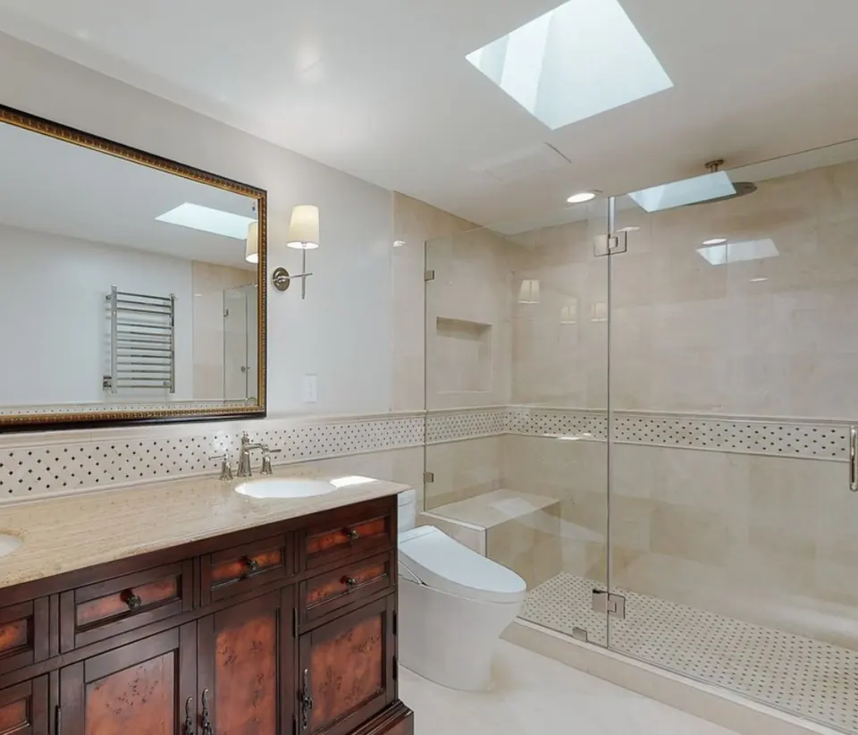 Primary bathroom remodel with a skylight, frameless glass shower, mosaic accent band, heated towel rail and a carved wood vanity