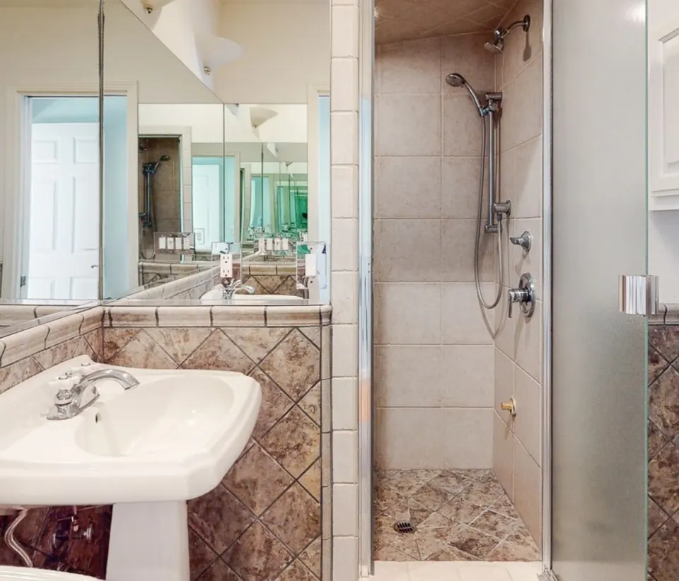 The bathroom before the remodel, with a pedestal sink and a dated tiled shower