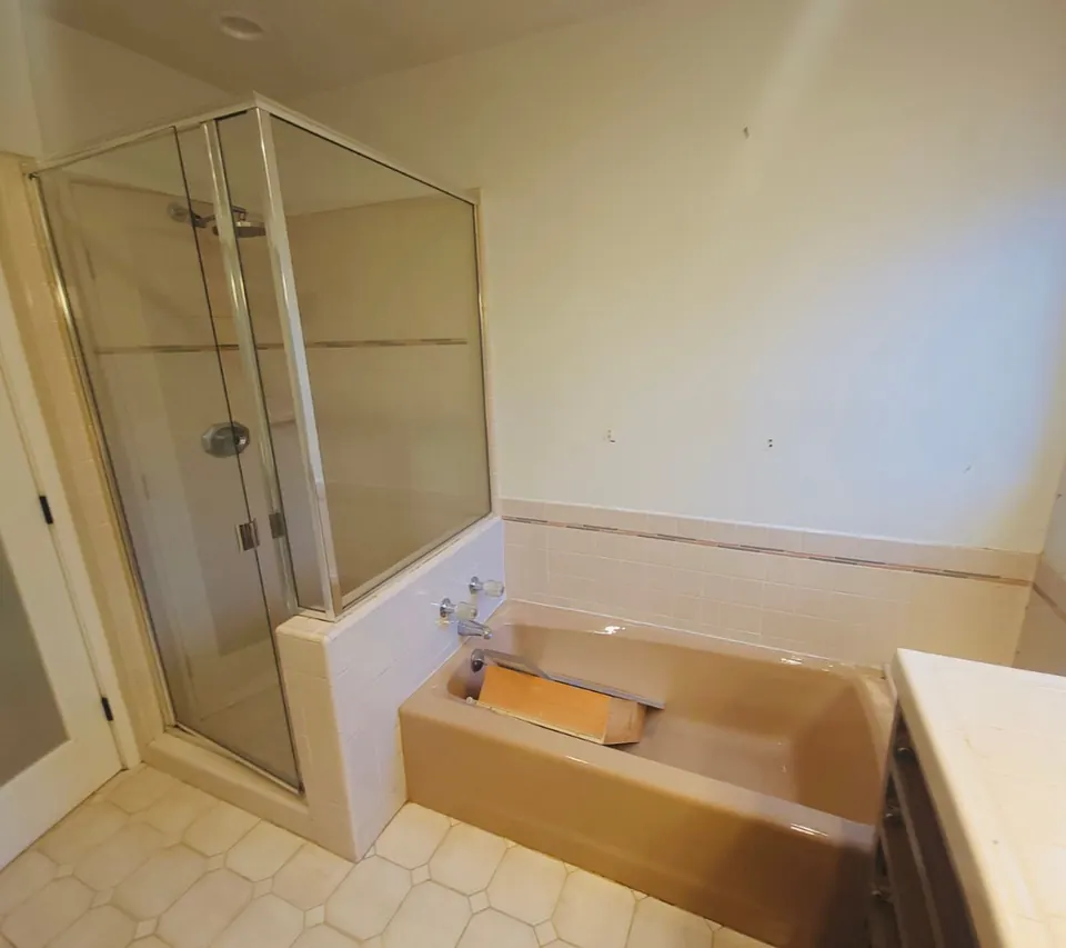 The same bathroom before the remodel, with a dated built-in tub deck and a framed glass shower