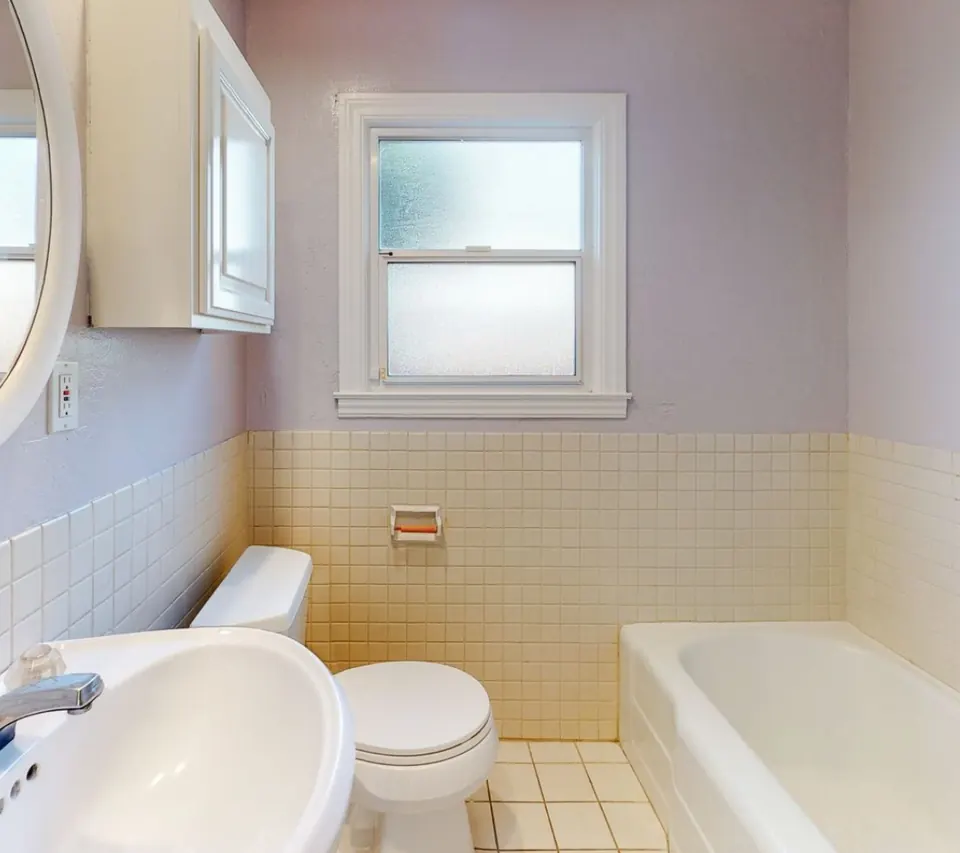 The bathroom before the remodel, with pink walls, yellow tile and an original tub