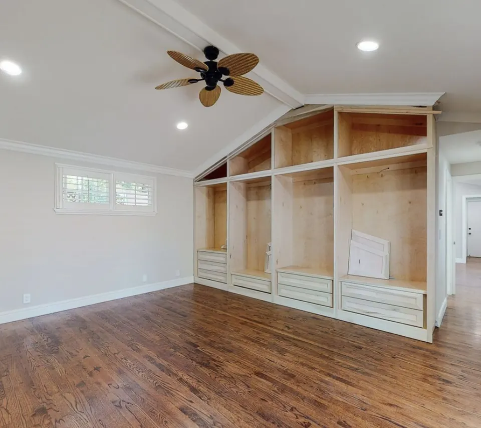 Bedroom with a vaulted ceiling and a full wall of custom built-in shelving and drawers replacing the old closet