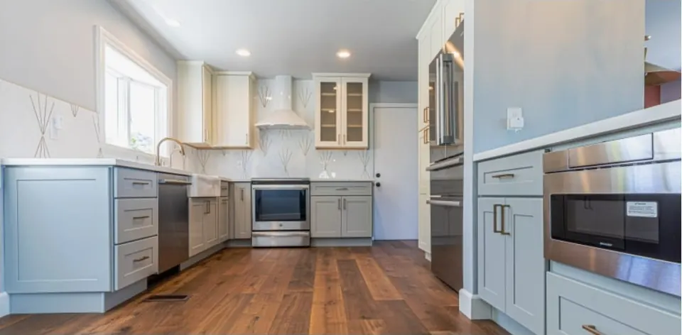 Remodeled kitchen with blue-gray shaker cabinets, white counters, stainless appliances and walnut floors
