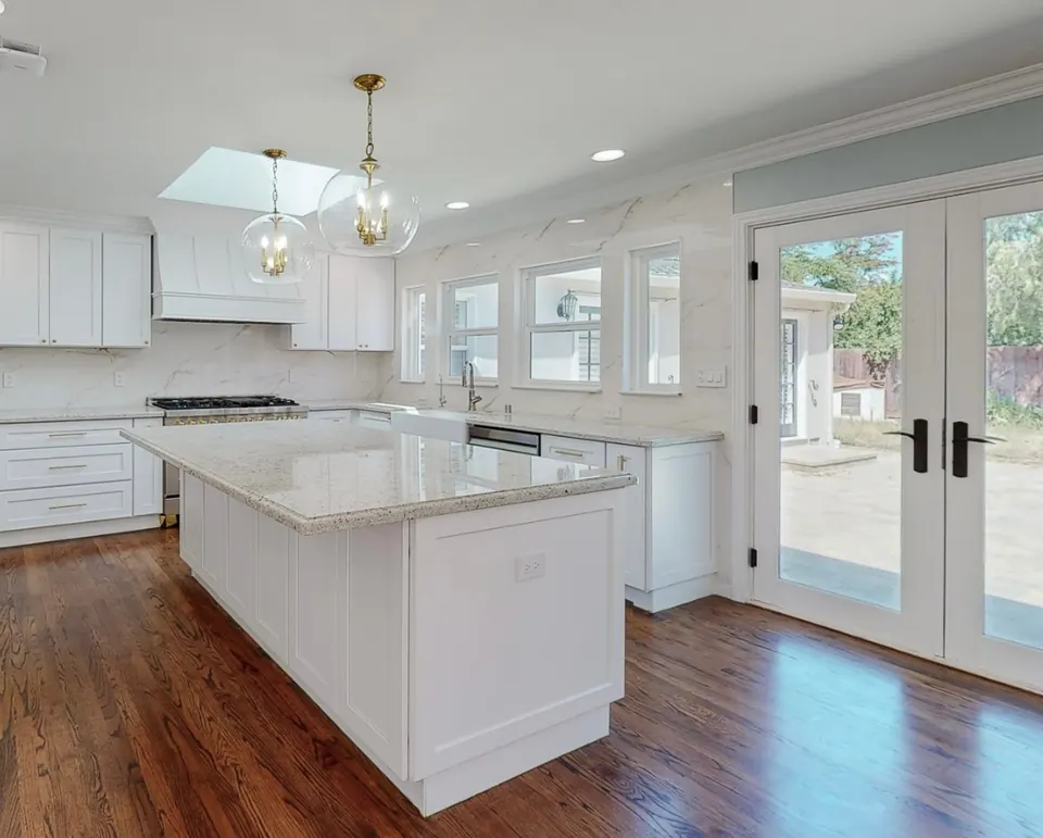 L-shaped kitchen remodel with white shaker cabinets, a marble-topped island, pendant lighting and French doors to the yard