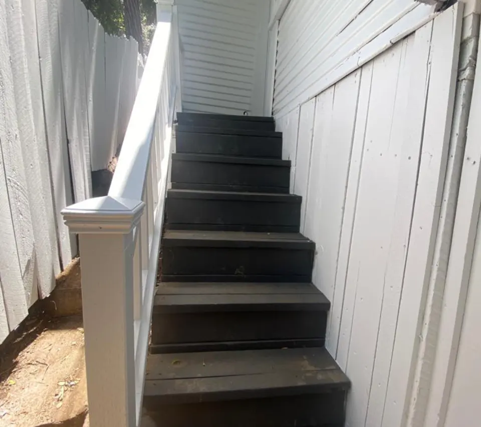 Rebuilt exterior side-yard staircase with dark painted treads and a new white handrail