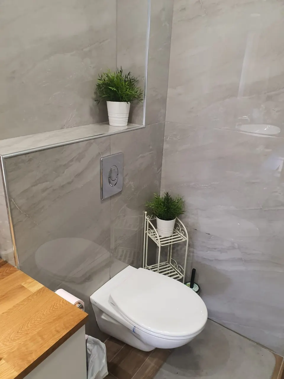 Fully tiled bathroom in large-format gray stone-look porcelain with a wall-hung toilet and a tiled display ledge