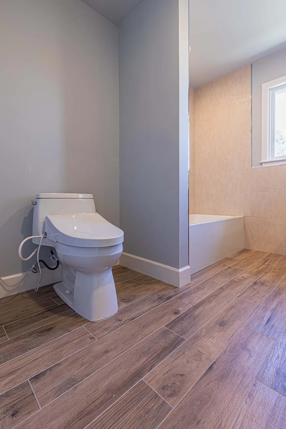 Bathroom with wood-look plank tile floors, a smart bidet toilet and a tub alcove in warm beige tile