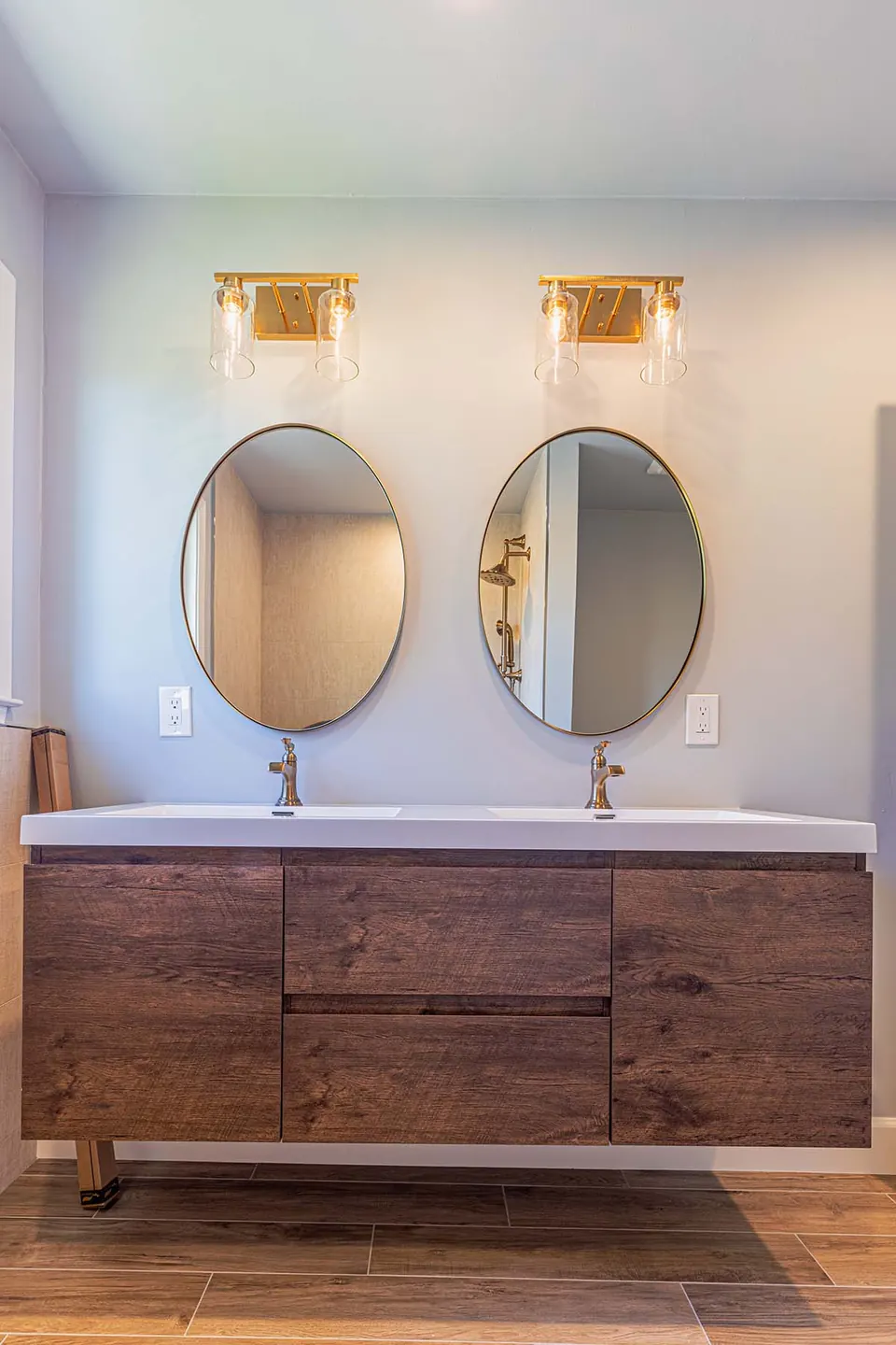 Walnut floating double vanity with two brass-framed oval mirrors and brass-and-glass sconces