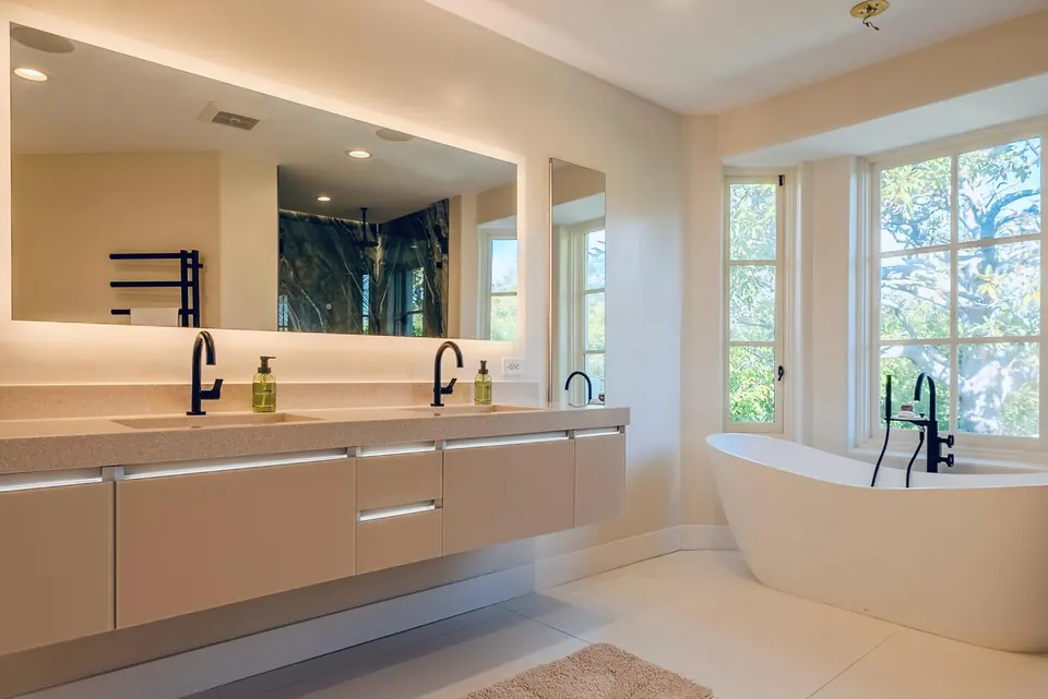 Floating double vanity with integrated under-lighting, a full-width backlit mirror and a freestanding tub beside it