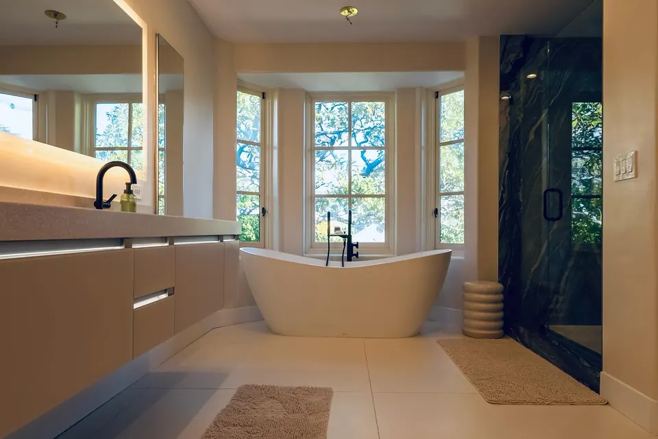 Wide view of a primary bathroom with a floating vanity, freestanding tub in a bay of windows and a green-marble walk-in shower