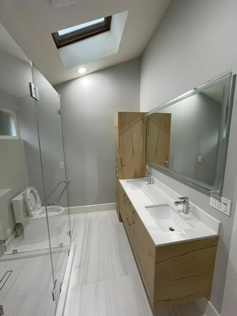 Long, narrow bathroom brightened by a skylight, with a frameless shower, oak vanity and large mirror