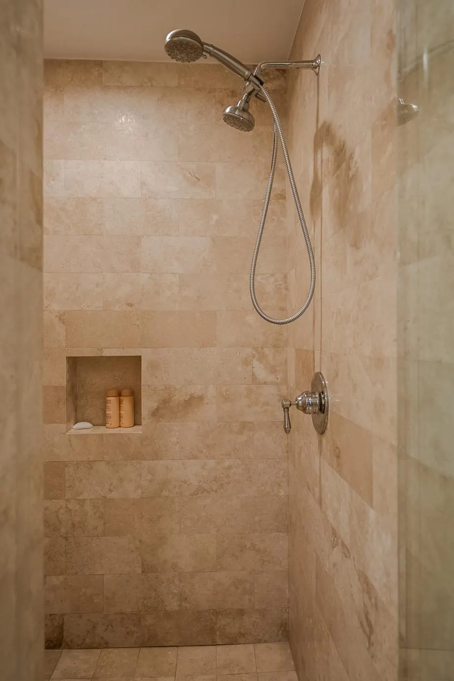 Walk-in shower clad in honed travertine with a recessed niche and brushed-nickel fixtures