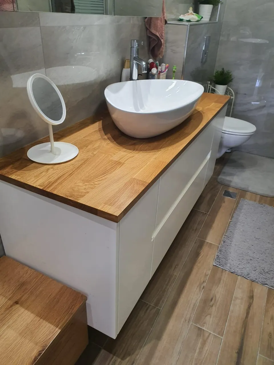 Bathroom vanity with a white vessel sink on a solid wood top, handleless white cabinets and wood-look tile floors