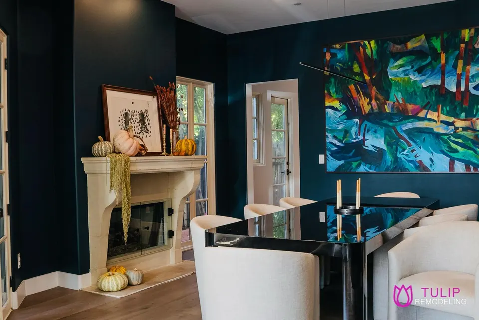 Dining room with deep-teal walls, a carved stone fireplace surround, a glass dining table and a large abstract painting
