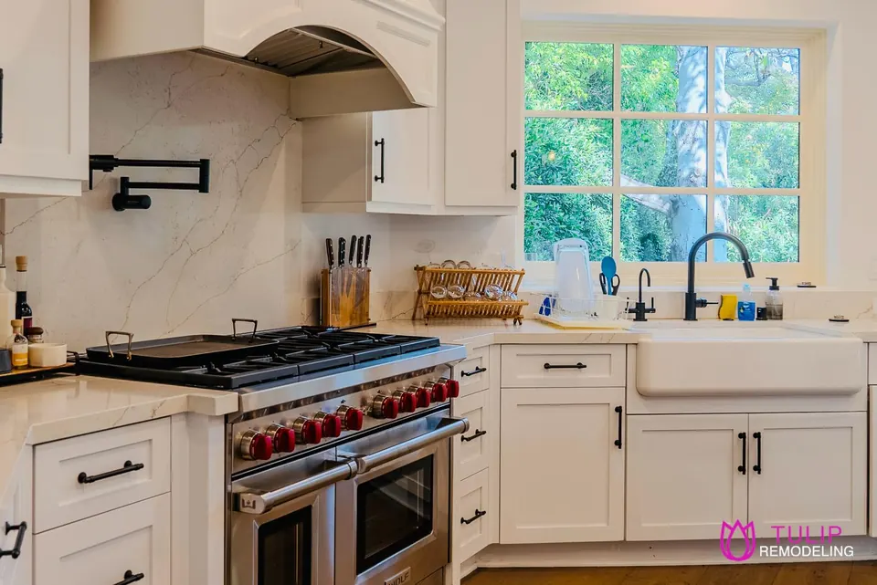 White shaker kitchen with a marble slab backsplash, wall-mounted pot filler, six-burner pro range and farmhouse sink