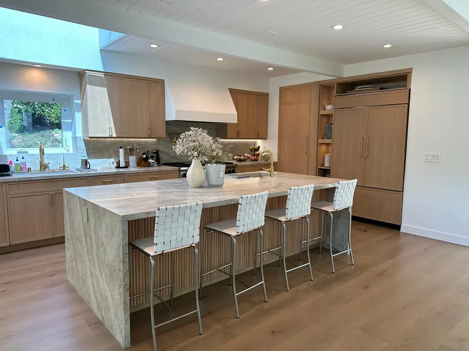 Open kitchen with a quartzite waterfall island seating four, rift-oak cabinetry, a paneled refrigerator and wide-plank oak floors