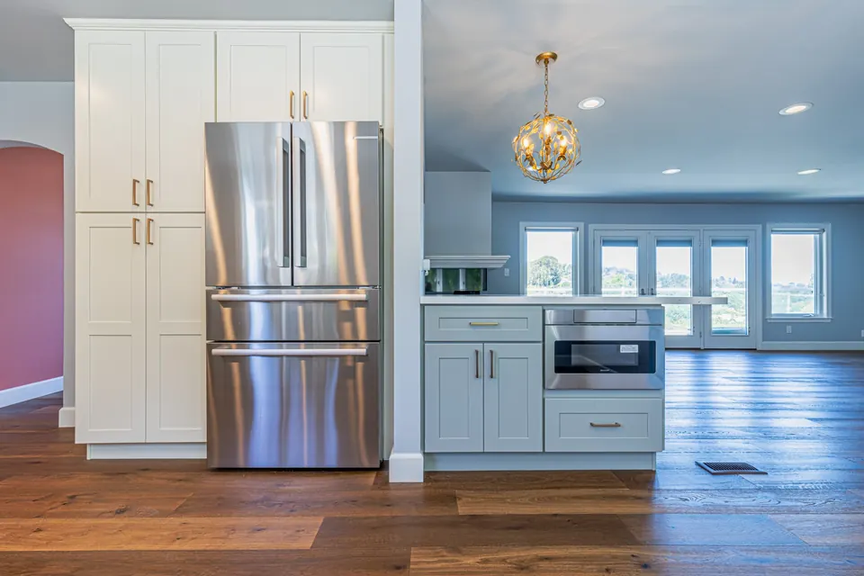 White and gray kitchen with tall pantry cabinets, a stainless French-door refrigerator and an island opening to the living room