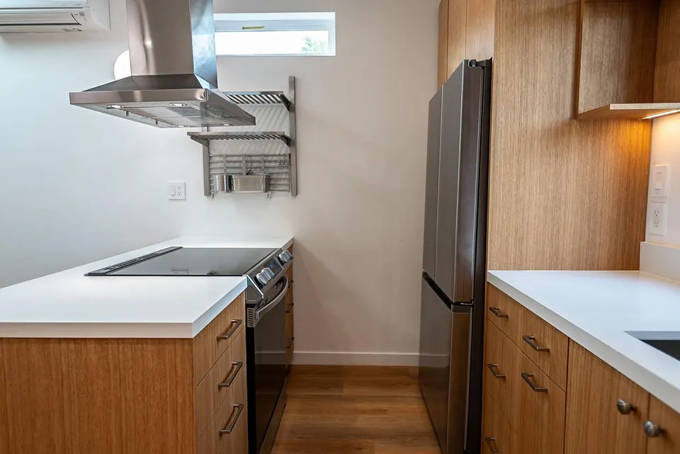 Kitchen range wall with a glass-top cooktop, stainless hood, rail storage and a tall stainless refrigerator