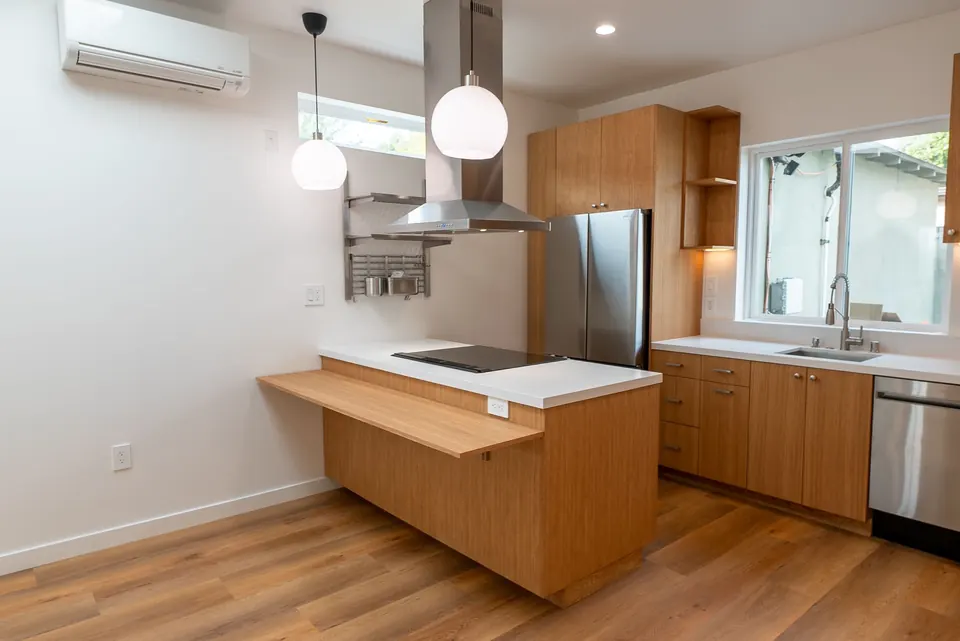 Kitchen peninsula with an induction cooktop, wood-veneer cabinets, pendant lights and a stainless refrigerator