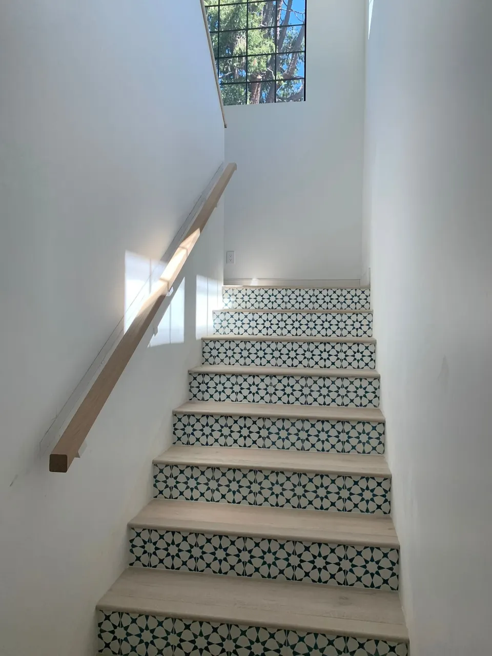 Interior staircase with patterned green-and-white tile risers, light wood treads and a wall-mounted handrail